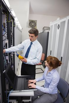 Team of technicians using digital cable analyser on servers in large data center