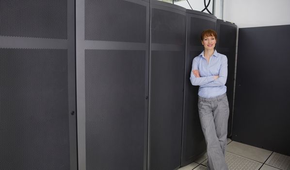 Pretty technician smiling at camera beside server towers in large data center