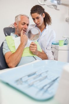 Patient showing dentist the problem in the mirror at the dental clinic