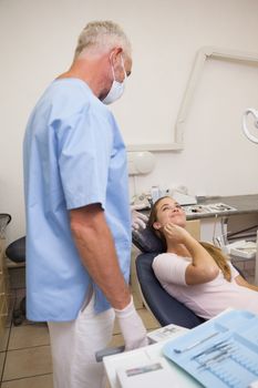 Patient lying in chair touching painful mouth looking at dentist at the dental clinic