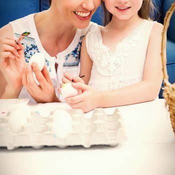 Mother and daughter painting easter eggs at home in the living room