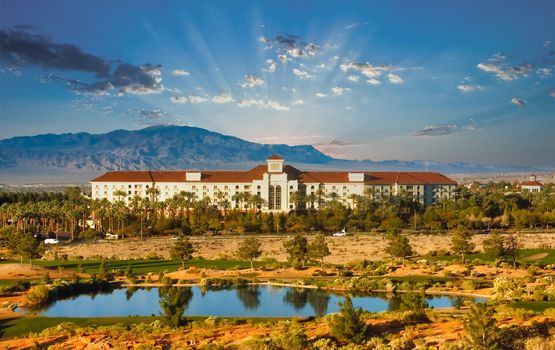 A stucco luxury resort with a red tile roof in the desert between a lake and a mountain