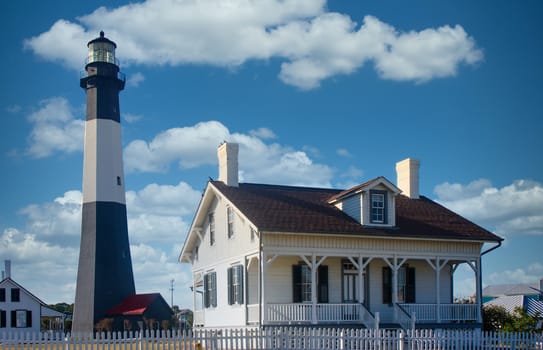 A white and black lighthouse rising into a clear blue sky next to a white clapboard coastal house