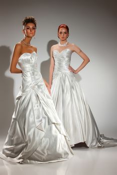 Two young beautiful women in wedding dresses on a studio background