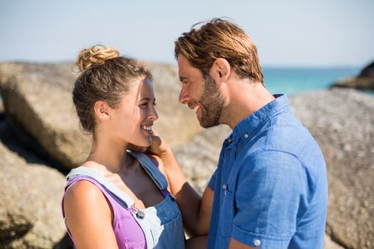 Side view of romantic young couple standing against rocks on beach