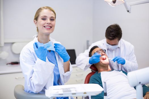 Dentist holding dental tool while her colleague examining patient in background at clinic