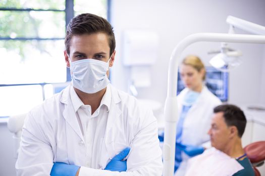 Portrait of dentist wearing surgical mask while his colleague examining patient in background