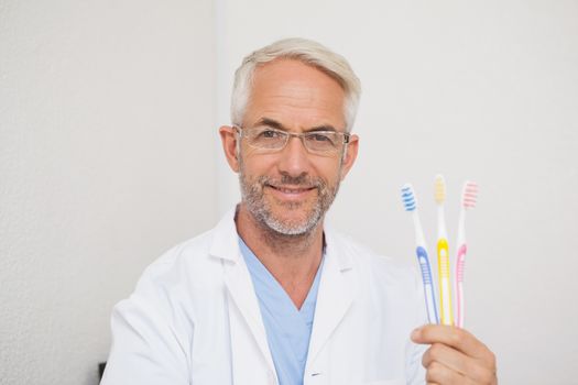 Dentist smiling at camera holding toothbrushes at the dental clinic