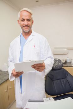 Dentist smiling at camera holding clipboard at the dental clinic