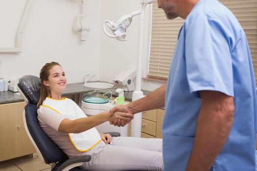 Dentist shaking hands with his patient in the chair at the dental clinic