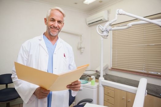 Dentist smiling at camera holding folder at the dental clinic