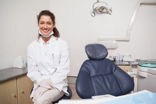 Dentist smiling at camera beside chair at the dental clinic