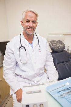 Dentist smiling at camera beside chair at the dental clinic