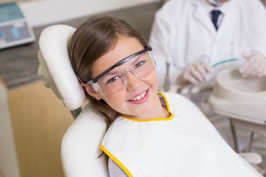 Little girl sitting in dentists chair wearing protective glasses at the dental clinic