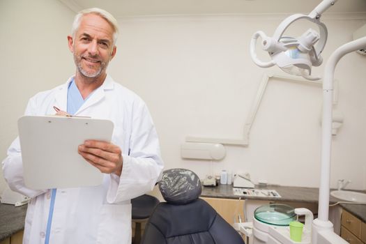 Dentist smiling at camera holding clipboard at the dental clinic