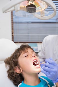 Pediatric dentist examining a little boys teeth in the dentists chair at the dental clinic