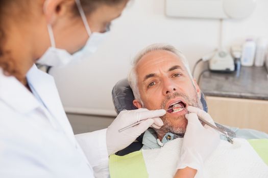 Dentist examining a patients teeth in the dentists chair at the dental clinic