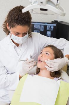 Pediatric dentist examining a patients teeth in the dentists chair at the dental clinic