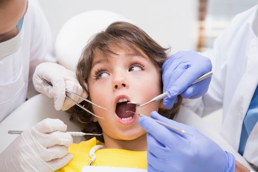 Pediatric dentist examining a little boys teeth with his assistant at the dental clinic