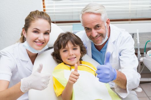 Pediatric dentist assistant and little boy all smiling at camera with thumbs up at the dental clinic