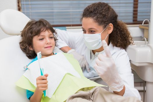 Pediatric dentist showing little boy in chair the toothrbrush at the dental clinic