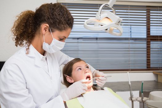 Pediatric dentist examining a little girls teeth in the dentists chair at the dental clinic