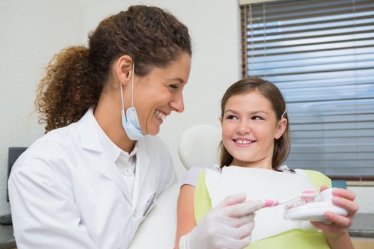 Pediatric dentist showing little girl how to brush her teeth at the dental clinic