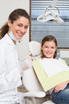 Pediatric dentist and little girl in the dentists chair smiling at camera at the dental clinic
