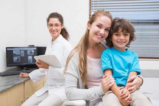 Pediatric dentist smiling at camera with little boy and his mother at the dental clinic