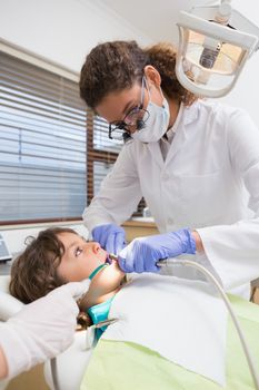 Pediatric dentist examining a little boys teeth in the dentists chair at the dental clinic