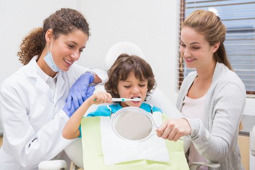 Pediatric dentist showing little boy how to brush teeth with his mother at the dental clinic