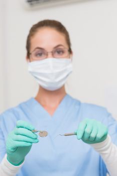 Dentist in blue scrubs holding tools looking at camera at the dental clinic
