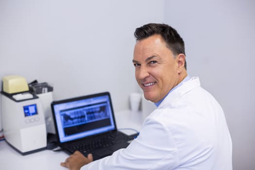 Portrait of happy dentist examining x-ray report on laptop in clinic