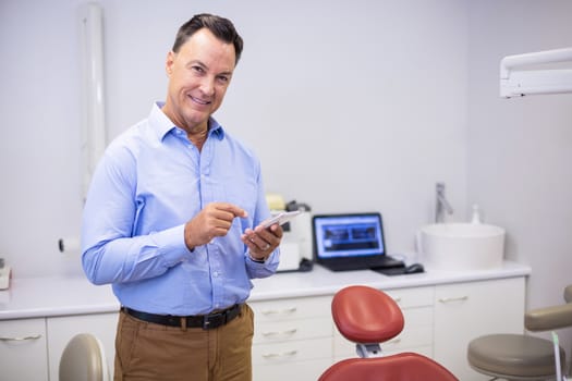 Portrait of smiling dentist using mobile phone in clinic