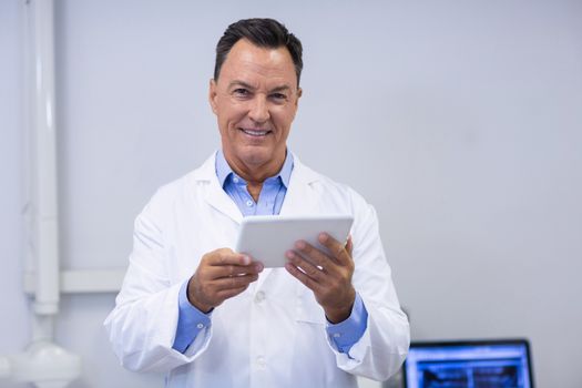 Portrait of smiling dentist holding digital tablet in dental clinic