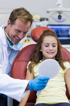 Smiling dentist showing mirror to young patient in dental clinic