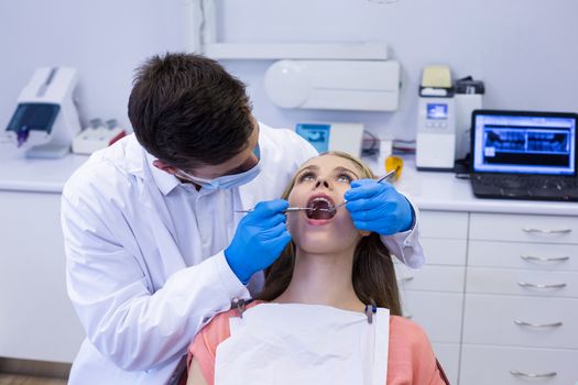 Dentist examining a female patient with tools in clinic