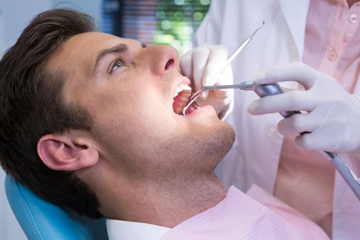 Close up of dentist holding medical equipment while giving treatment to patient at clinic