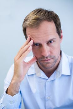 Portrait of tensed dentist sitting with hand on forehead in clinic