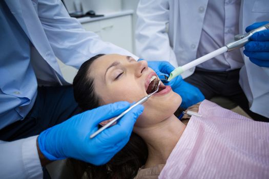 Dentist examining a female patient with tools at dental clinic