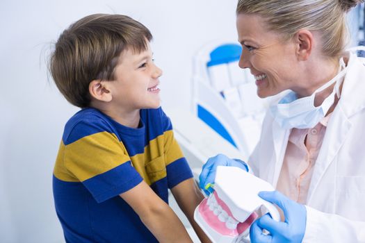 Happy dentist holding dental mold while looking at boy in clinic