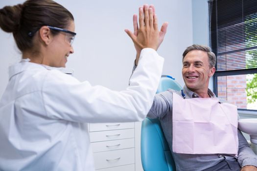 Happy dentist giving high five to man at medical clinic