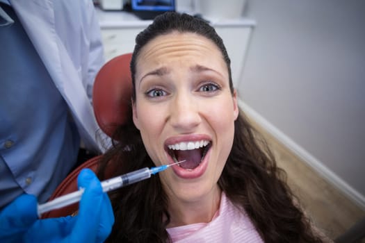 Dentist injecting anesthetics in scared female patient mouth at dental clinic