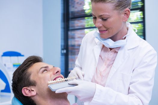 Smiling dentist holding equipment while examining patient at medical clinic