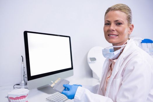 Portrait of dentist working while sitting by computer at clinic
