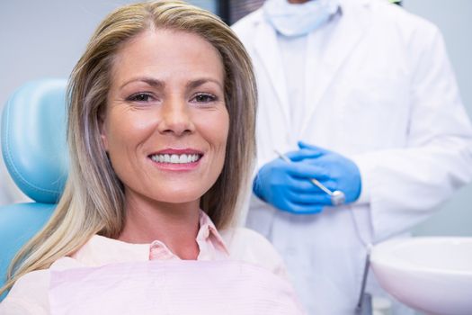 Portrait of patient sitting on chair against dentist at medical clinic