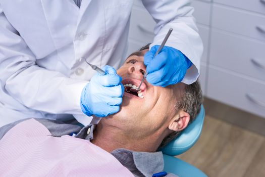 High angle view of dentist giving dental treatment to man at clinic