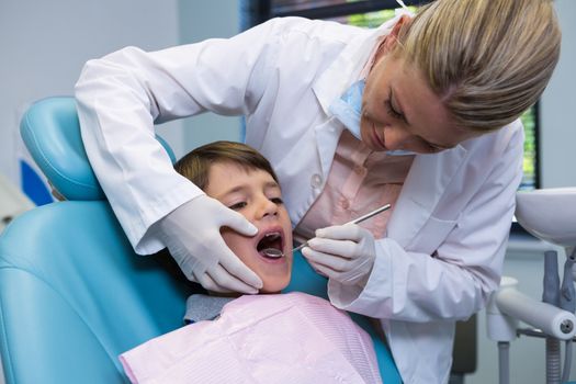 Dentist holding equipment while examining boy at medical clinic