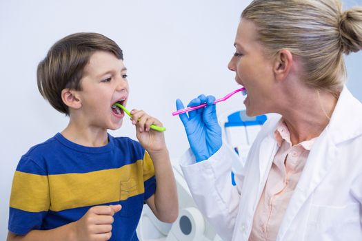 Dentist and boy brushing teeth against wall at clinic 