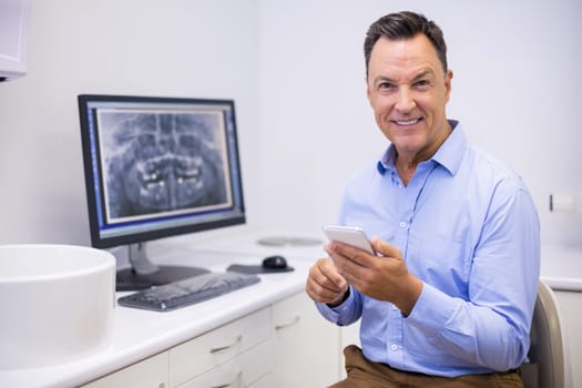 Portrait of happy dentist using mobile phone in clinic
